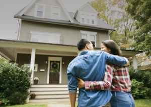 Couple embrace in front of new home.